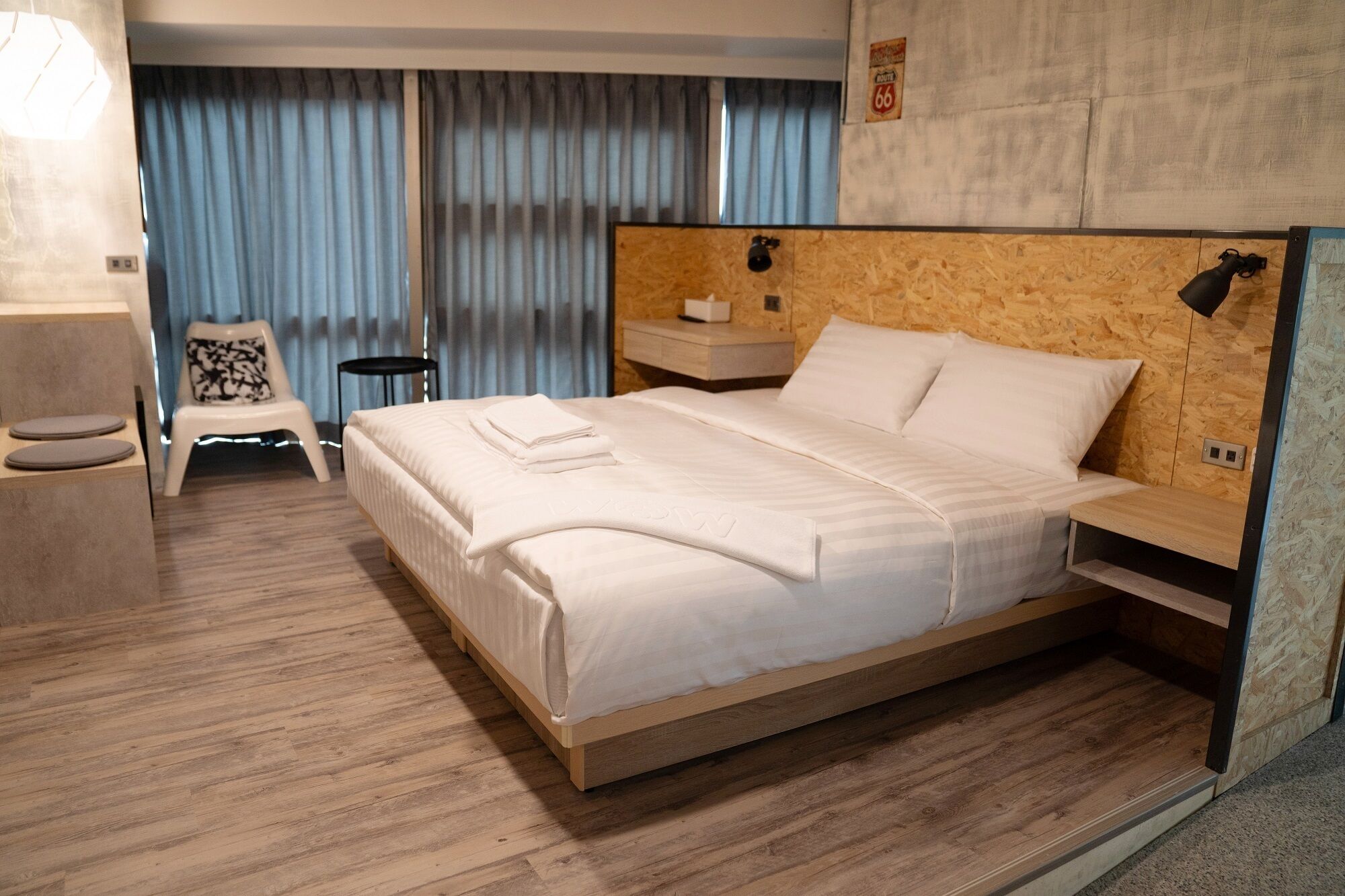 Une chambre d’hôtel moderne avec un lit en bois, une petite table de chevet, une chaise et une commode.