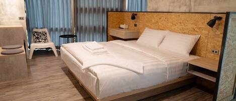 A modern hotel room with a wooden bed, a small bedside table, a chair, and a nightstand.