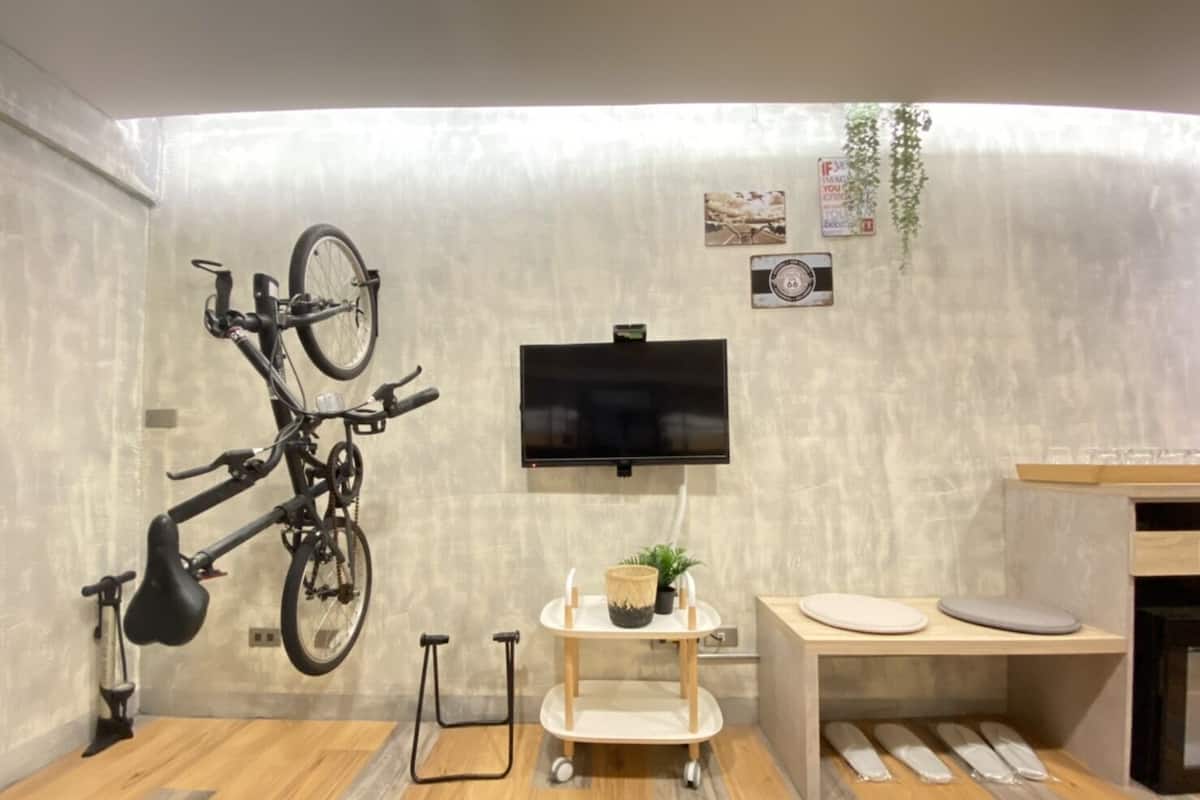 Ein modernes Zimmer mit einem angebrachten Fahrrad, einem Fernseher, einer kleinen Pflanze und einer hölzernen Bank.