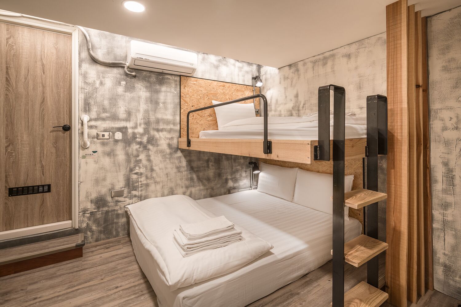 Una cama litera con una plataforma de madera, una cama individual abajo y un estante de madera pequeño.