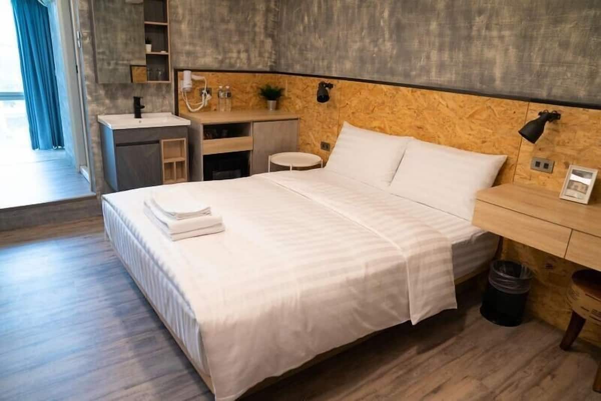 Ein modernes Hotelzimmer mit einem großen Bett, einem kleinen Schreibtisch, einem Schminktisch und Blick ins Freie.
