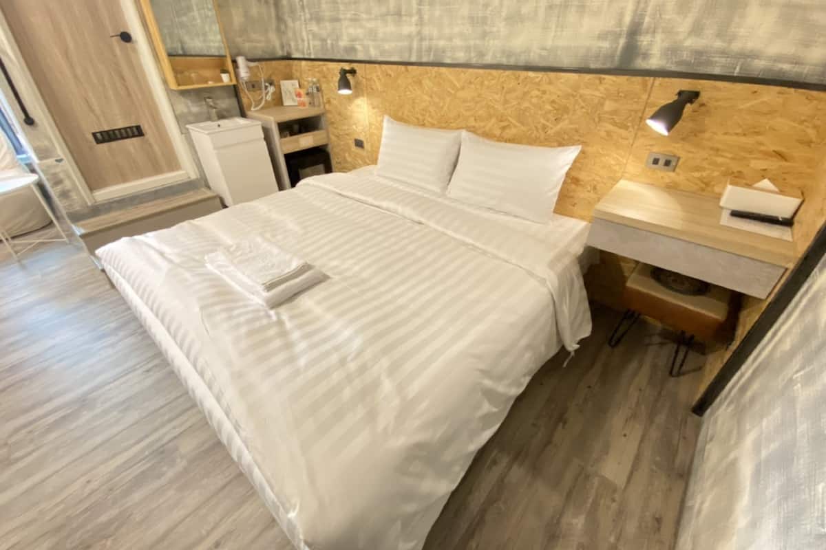 Ein ordentlich bezogenes Bett mit weißen Leinen, ein Nachttisch mit Lampe und ein Holz-Kopfteil.