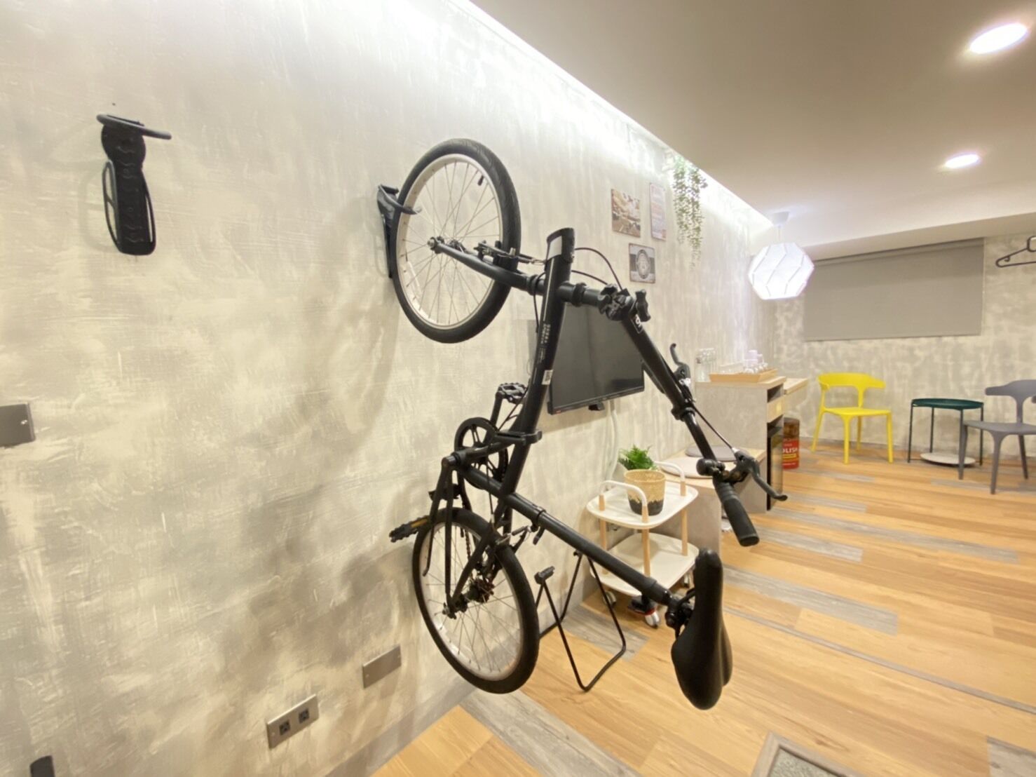 A room with a wall-mounted bicycle, a small table with a plant, and a yellow chair.