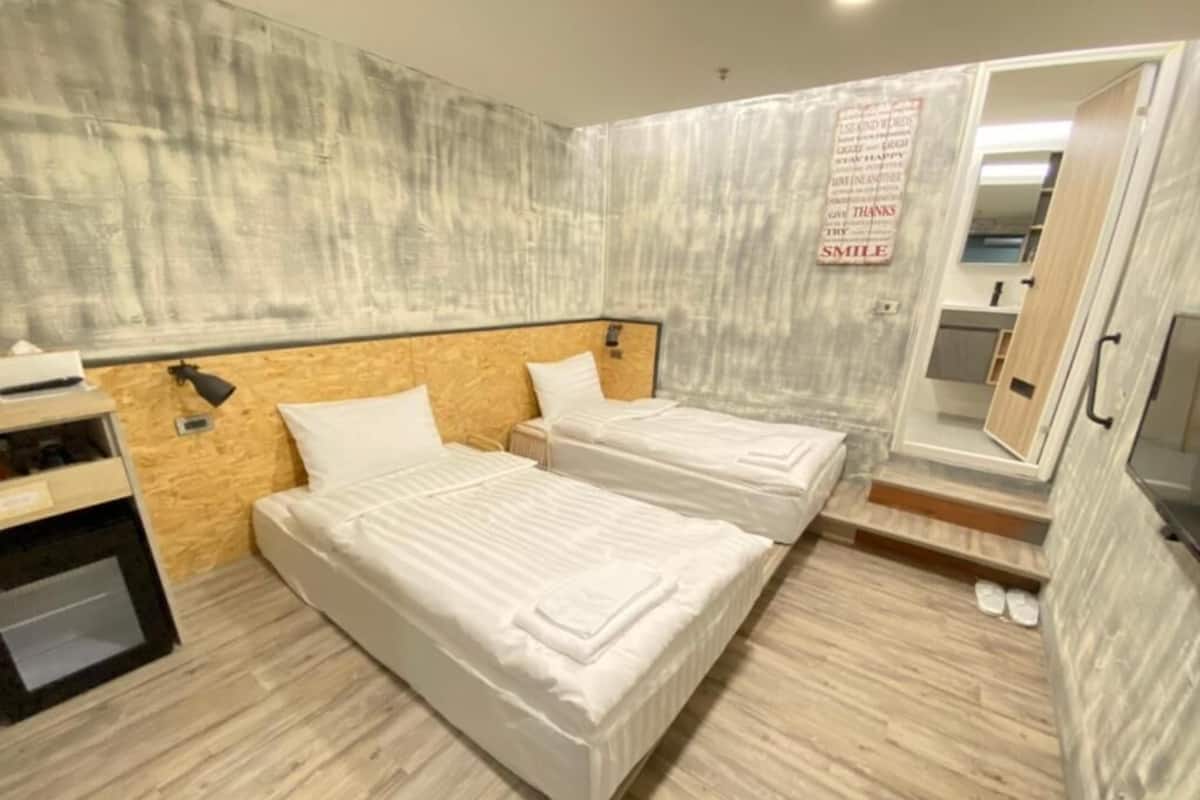 Ein Hotelzimmer mit zwei Betten, einem Holzkopfstück, einem kleinen Schreibtisch und einem Spiegel.