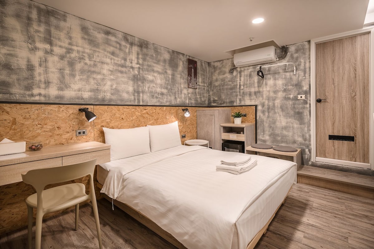 Ein modernes Schlafzimmer mit einem Holz-Kopfteil, einem Bett mit weißer Bettwäsche, einem Schreibtisch mit Stuhl und einem eingebauten Kleiderschrank.