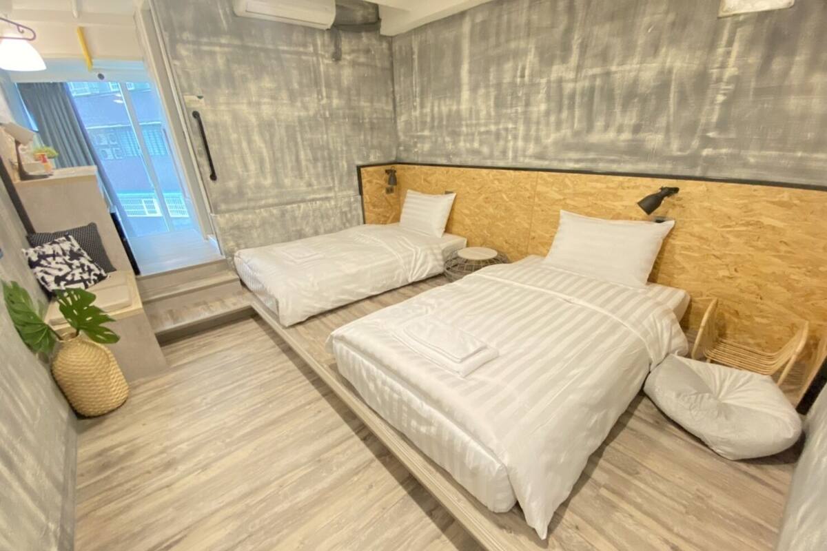 Ein modernes Hotelzimmer mit zwei Betten, einem Holzkopfende, einer kleinen Pflanze und Blick auf die Stadt durch das Fenster.