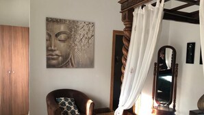 Ein Schlafzimmer mit einem Himmelbett, einem Holzschrank, einem Sessel mit gemustertem Kissen und einem großen Wandbild.