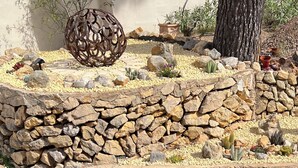 Ein Garten mit einer Steinmauer, verschiedenen Pflanzen und einer Zierfigur aus Metall.