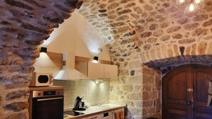 A kitchen with stone walls, a wooden door, and modern appliances. - Bel Appartement en sud Ardèche au Bord de la Rivière (Ucel)