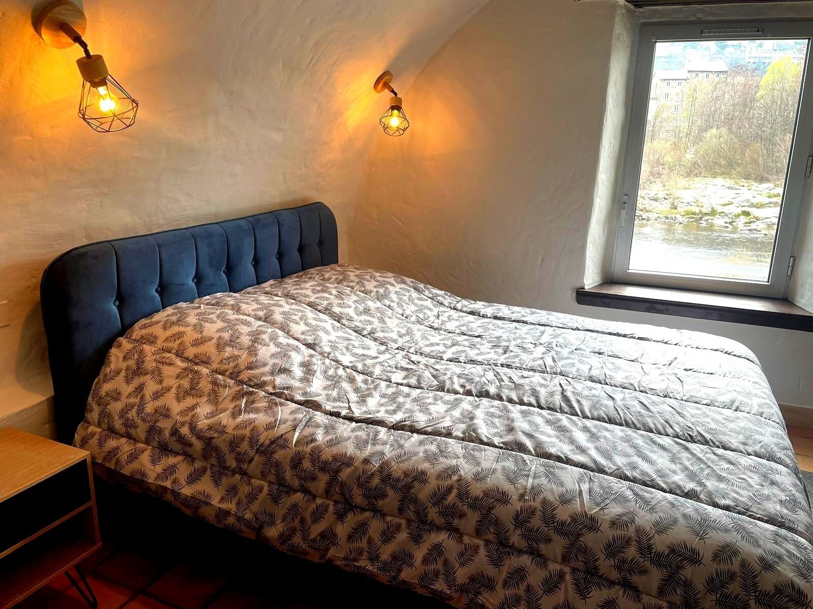 A bedroom with a tufted headboard, a patterned bedspread, and two wall-mounted light fixtures.