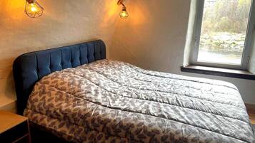 A bedroom with a tufted headboard, a patterned bedspread, and two wall-mounted light fixtures.