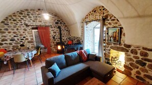 A cozy room with a stone wall, a sofa, a dining table, and a fireplace. - Bel Appartement en sud Ardèche au Bord de la Rivière (Ucel)