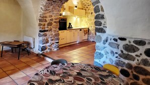 A cozy room with a stone archway leading to a kitchen. There is a dining table with chairs, a patterned rug, and a bed with a yellow pillow. - Bel Appartement en sud Ardèche au Bord de la Rivière (Ucel)
