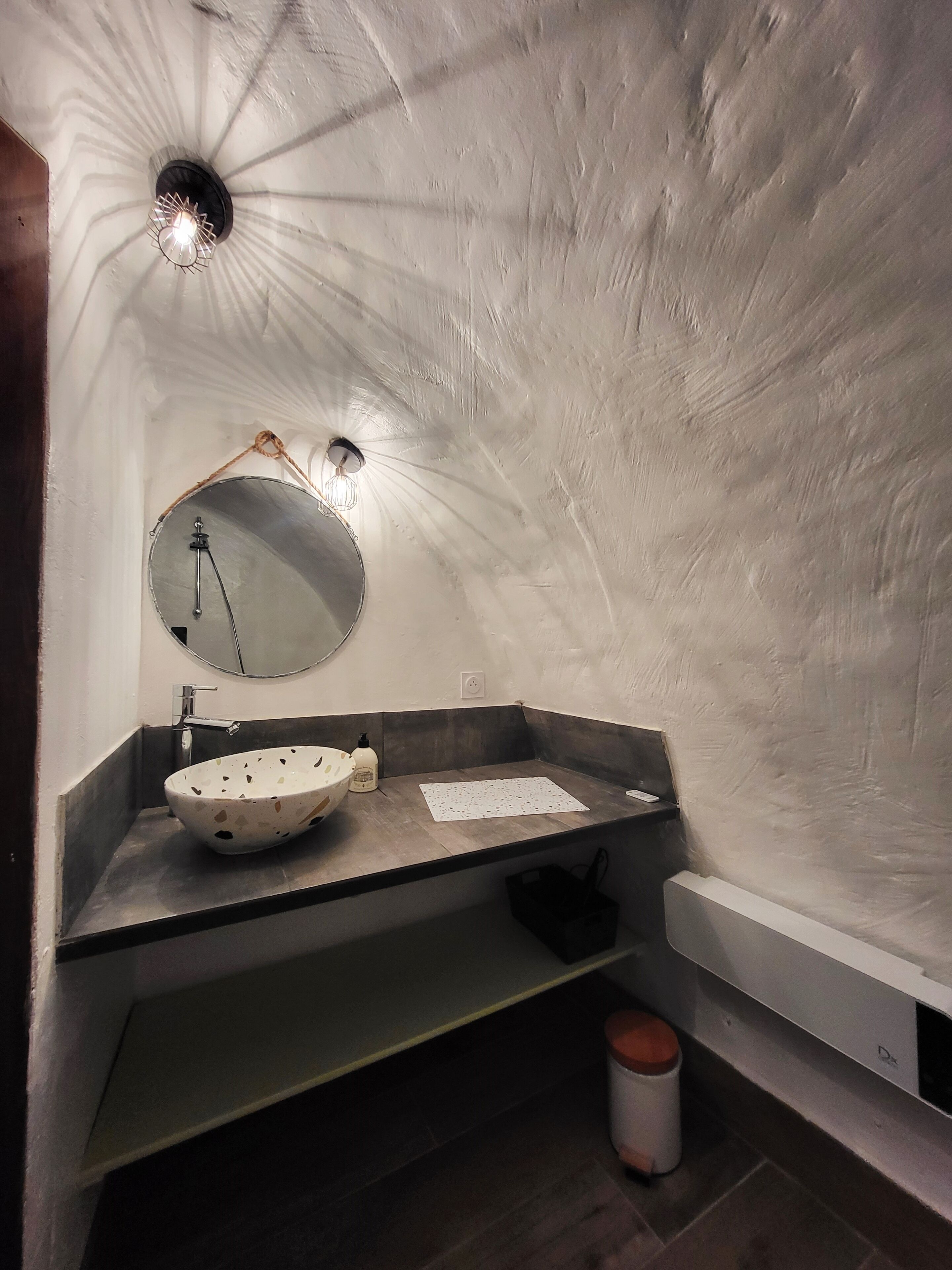 Une salle de bain avec un miroir rond, un lavabo sur colonne et un porte-serviettes.