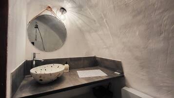 Une salle de bain avec un miroir rond, un lavabo sur colonne et un porte-serviettes.