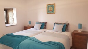 A double bed with a teal and white duvet, two bedside tables with lamps, a framed artwork on the wall, and a window with curtains. - House in the historic center  (BELMONTE)