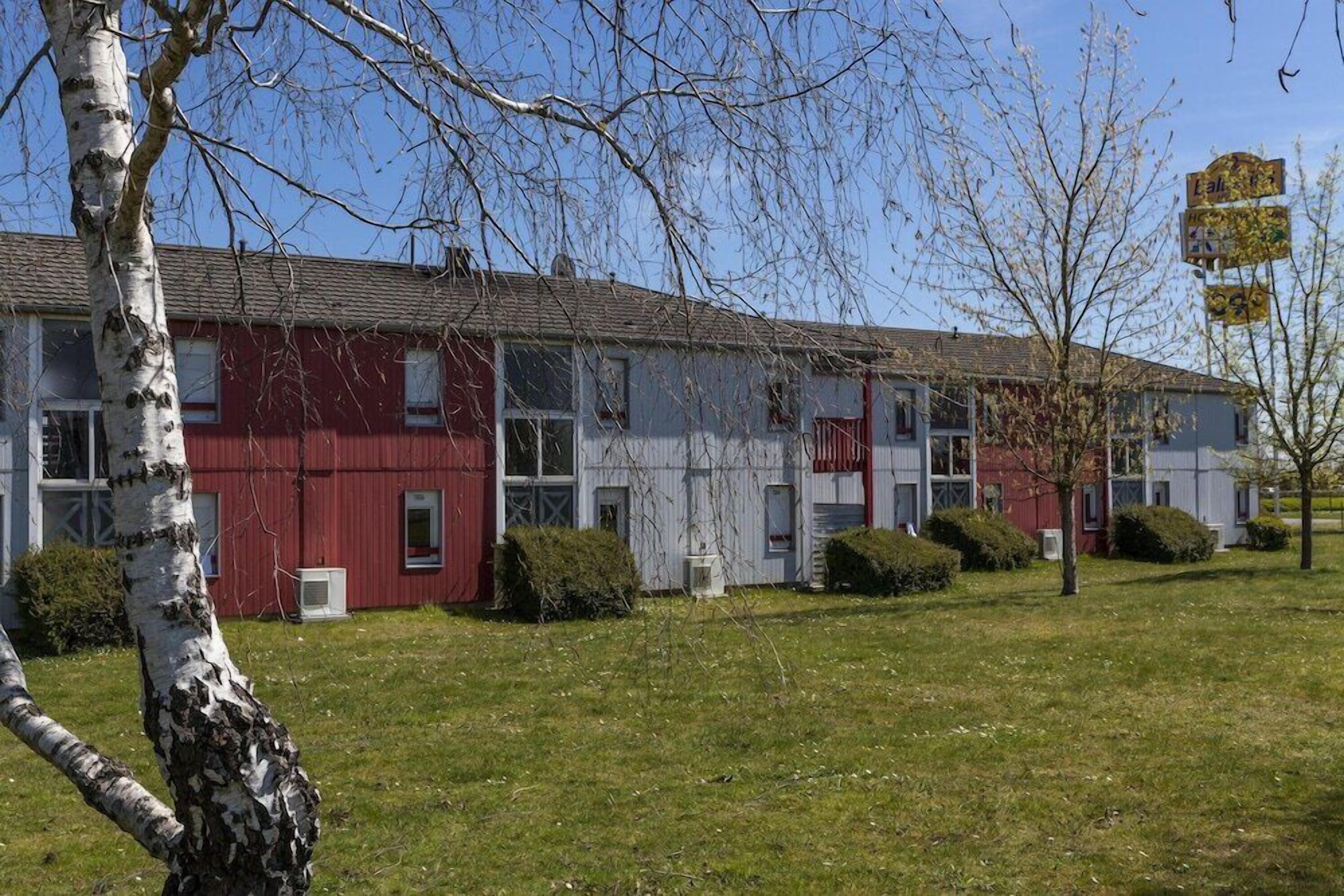 Ein zweistöckiges Gebäude mit roter und weißer Fassade, zahlreichen Fenstern und einem grünen Rasen.