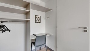A compact room with a desk, chair, and a coat rack with hangers.