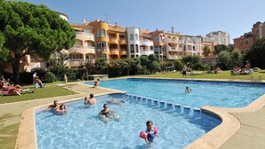 Ein Swimmingpool, umgeben von mehrstöckigen Gebäuden mit Balkonen, einer Rasenfläche mit Liegestühlen und einem strahlend blauen Himmel.