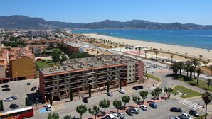 Eine Küstenstadt mit Strand, ein mehrstöckiges Hotel mit Balkonen und einem klaren, blauen Himmel.