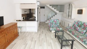 A modern living room with a sofa, a glass coffee table, and a wooden cabinet. There is a staircase leading to an upper floor.