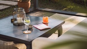 Una mesa con un vaso de jugo de naranja, un vaso de vino blanco, una vela en un frasco y una libreta.