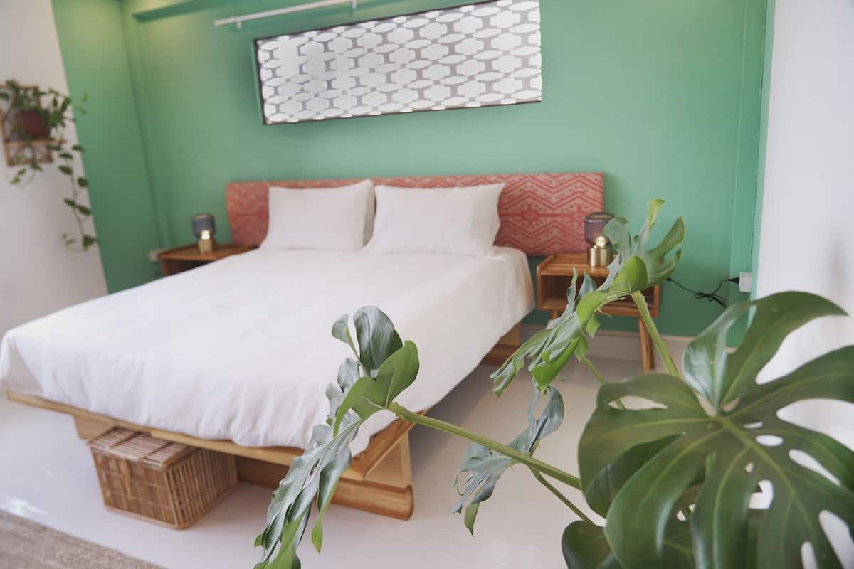A bedroom with a bed, a nightstand, a wall-mounted light, and a potted plant.