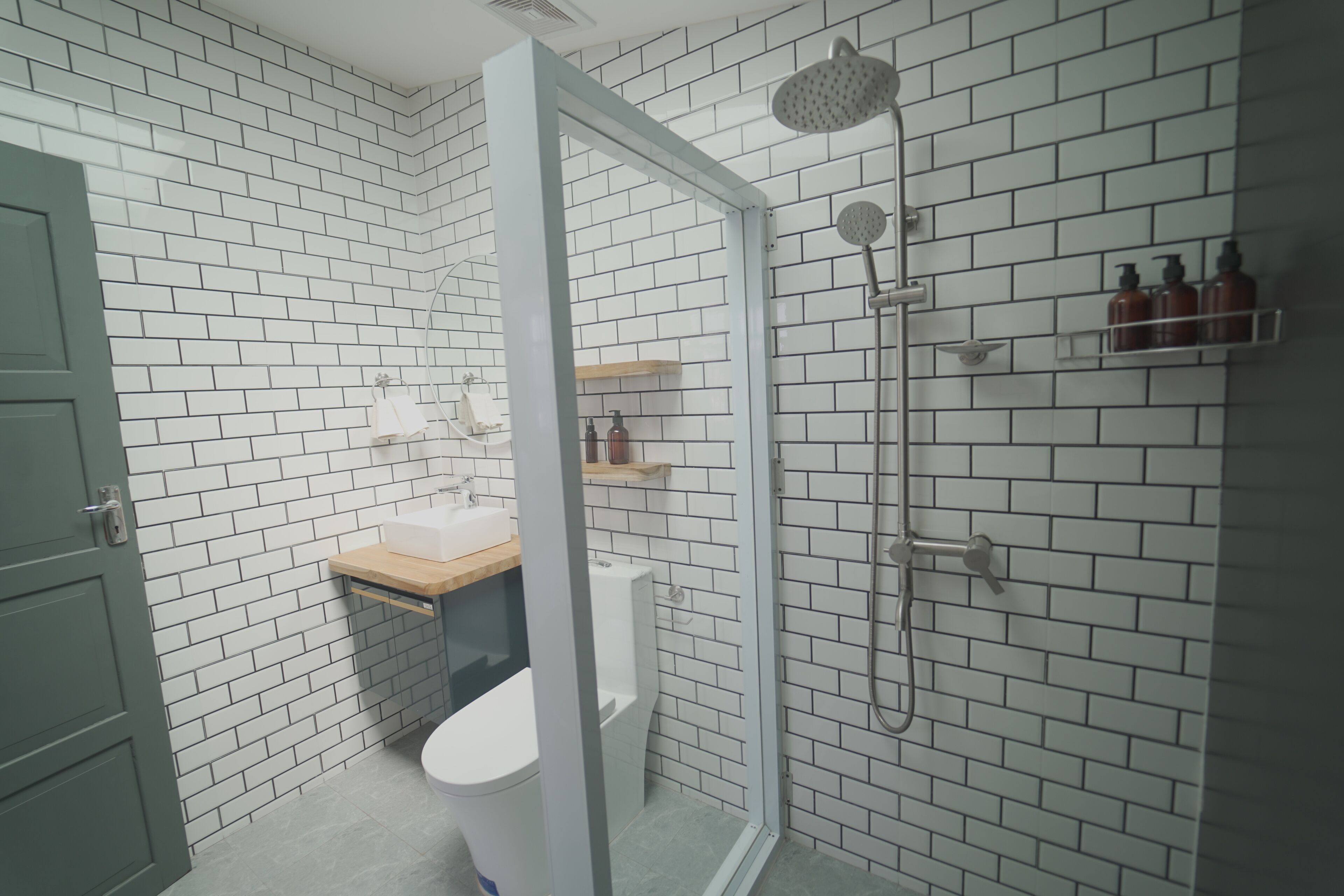 A bathroom with white brick walls, a glass shower enclosure, a toilet, and a sink with a wooden countertop.