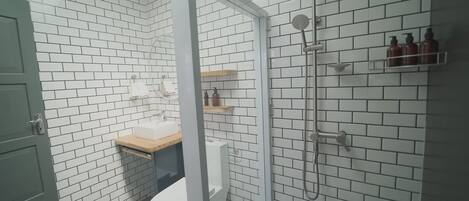 A bathroom with white brick walls, a glass shower enclosure, a toilet, and a sink with a wooden countertop.