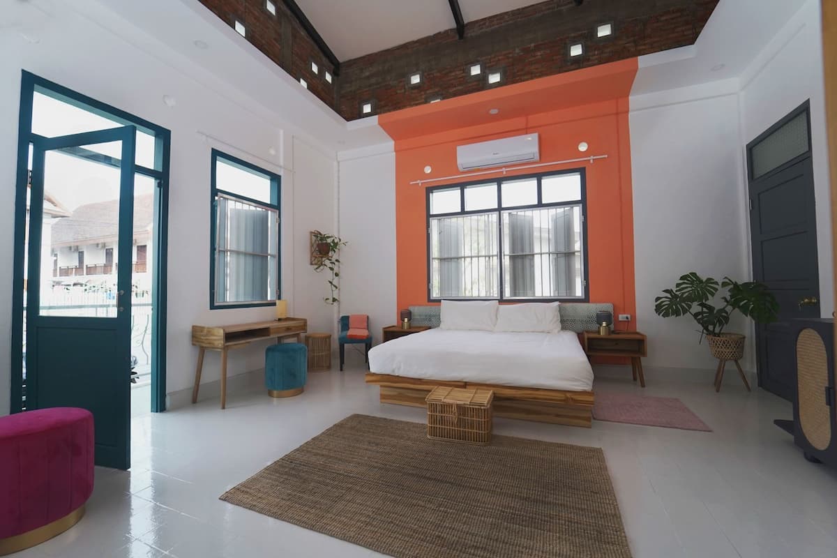 A modern bedroom with a large bed, a desk, a chair, and a potted plant.