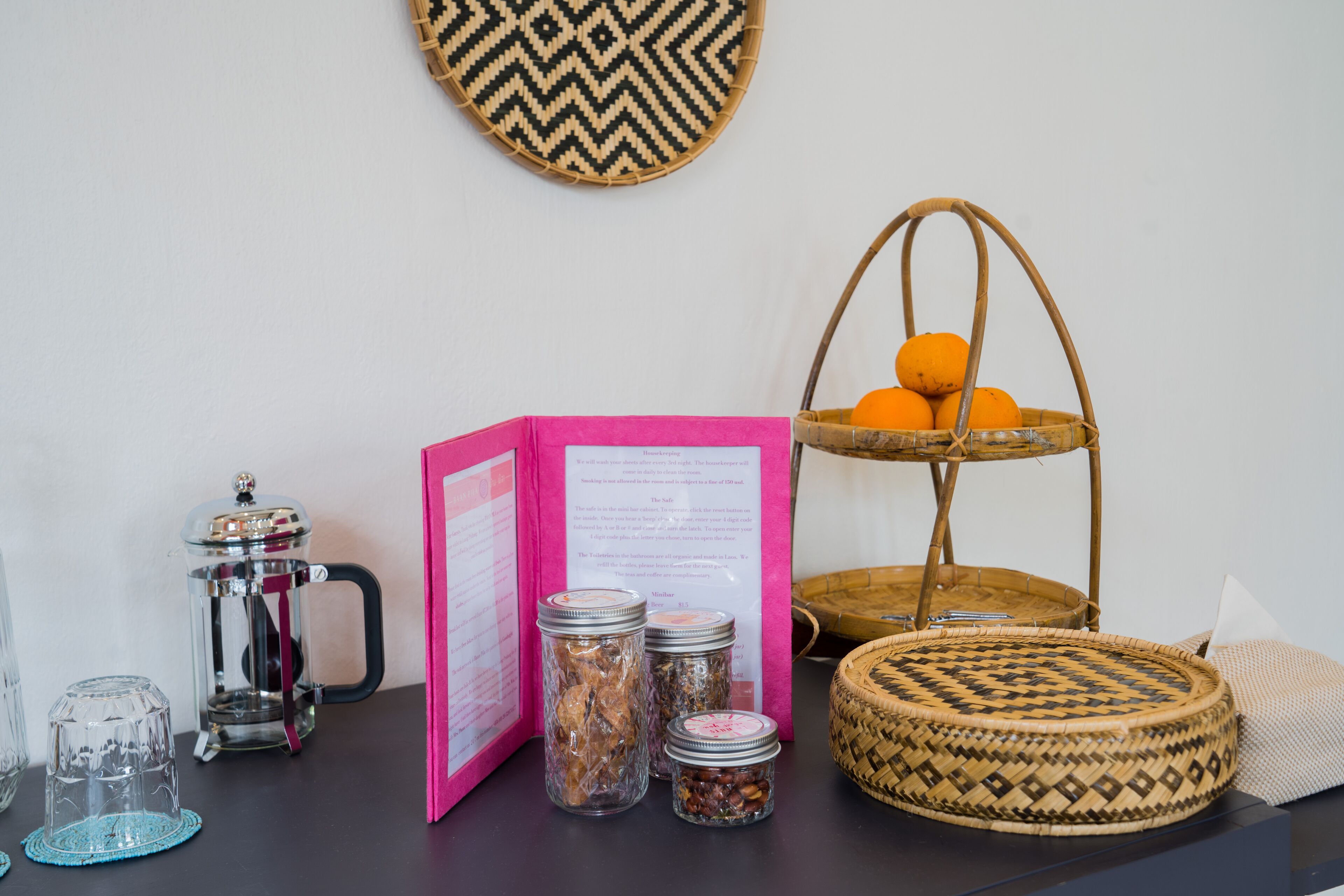 A table with a coffee maker, jars, a basket with oranges, and a woven basket.