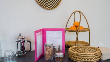 A table with a coffee maker, jars, a basket with oranges, and a woven basket.