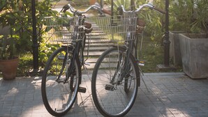 Una bicicleta estacionada en un espacio exterior sombreado, con plantas en macetas y una pared blanca al fondo.
