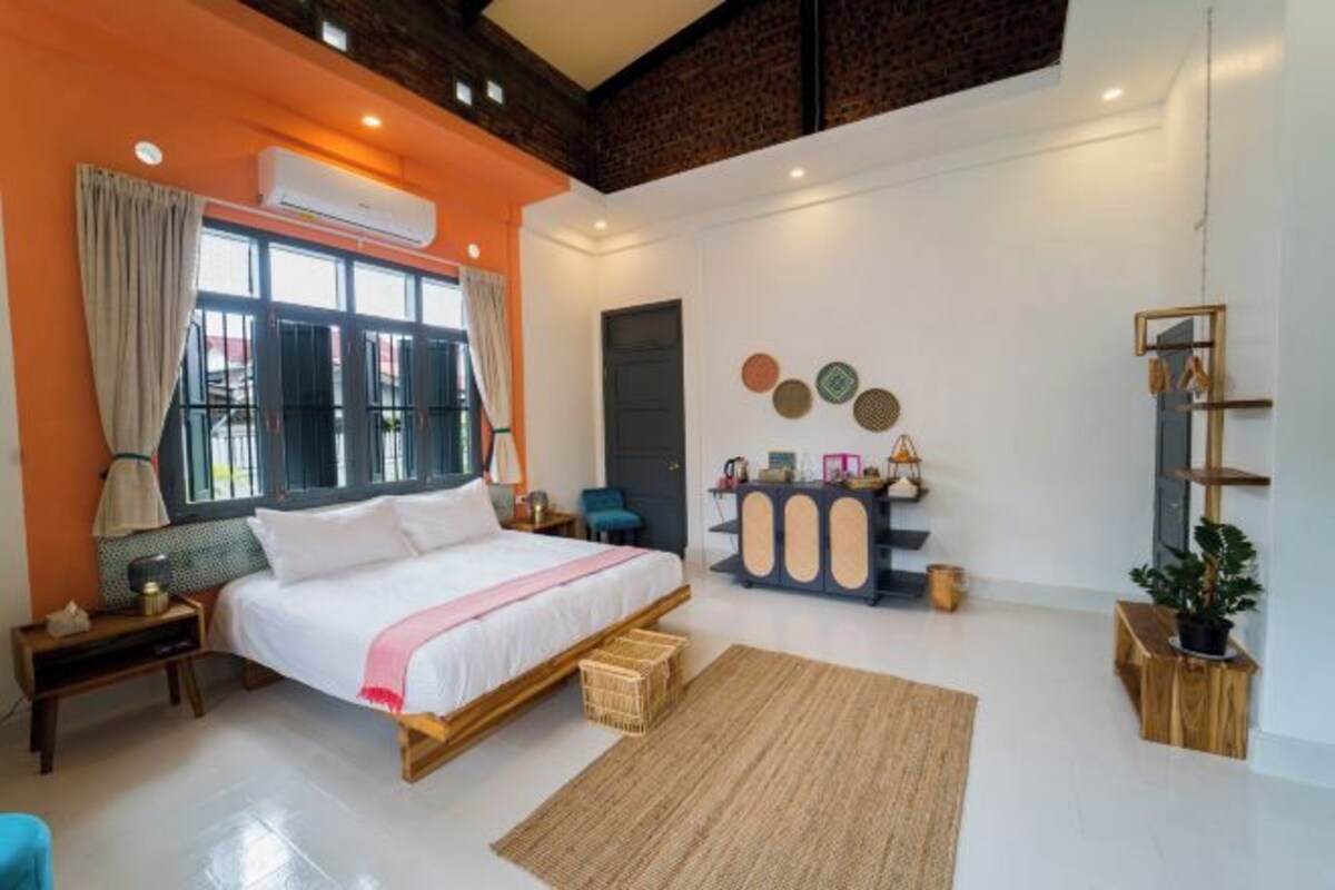 A modern bedroom with a large bed, a wooden nightstand, a bedside table, a wall-mounted shelf, and a large window with curtains.