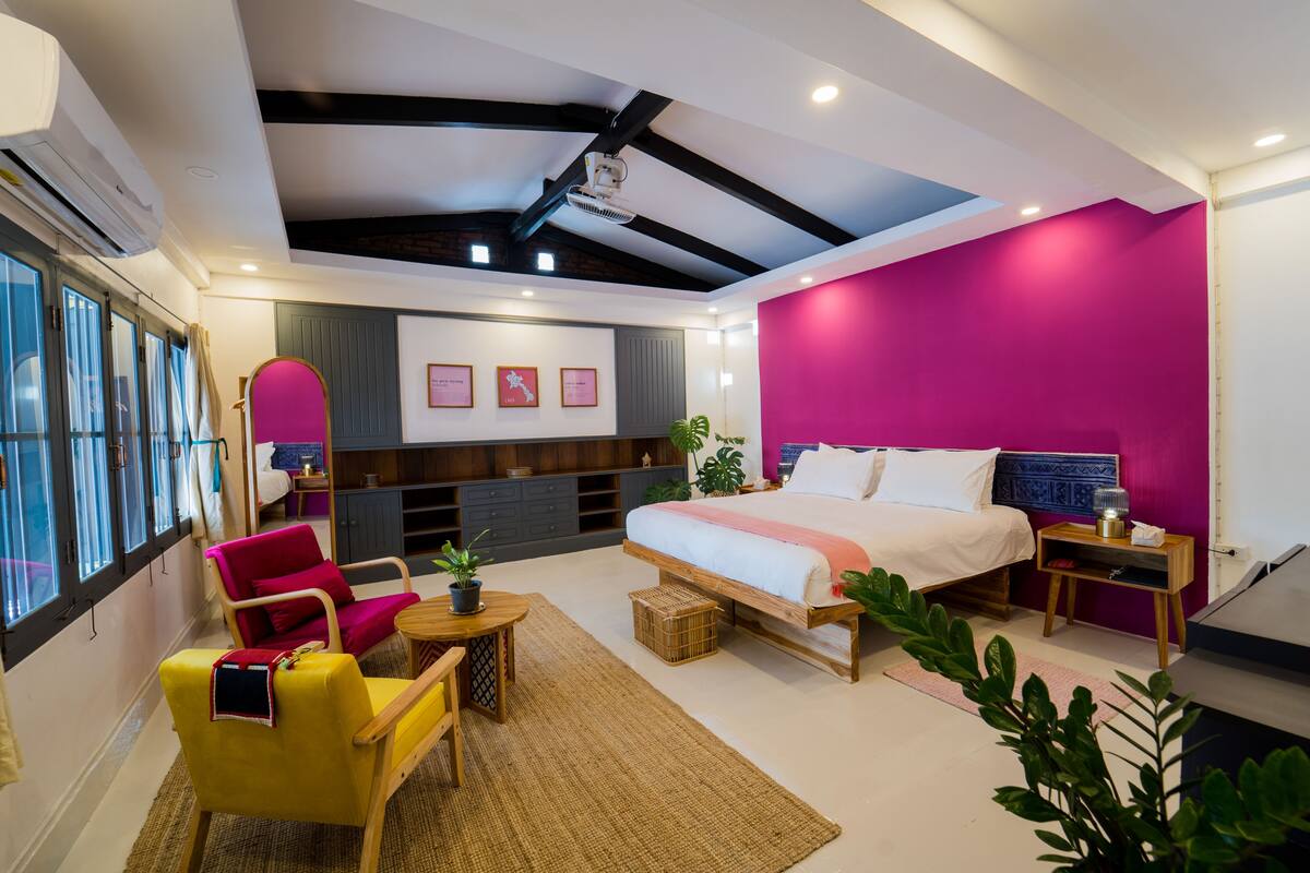A modern bedroom with a large bed, a desk, a chair, and a window with curtains.