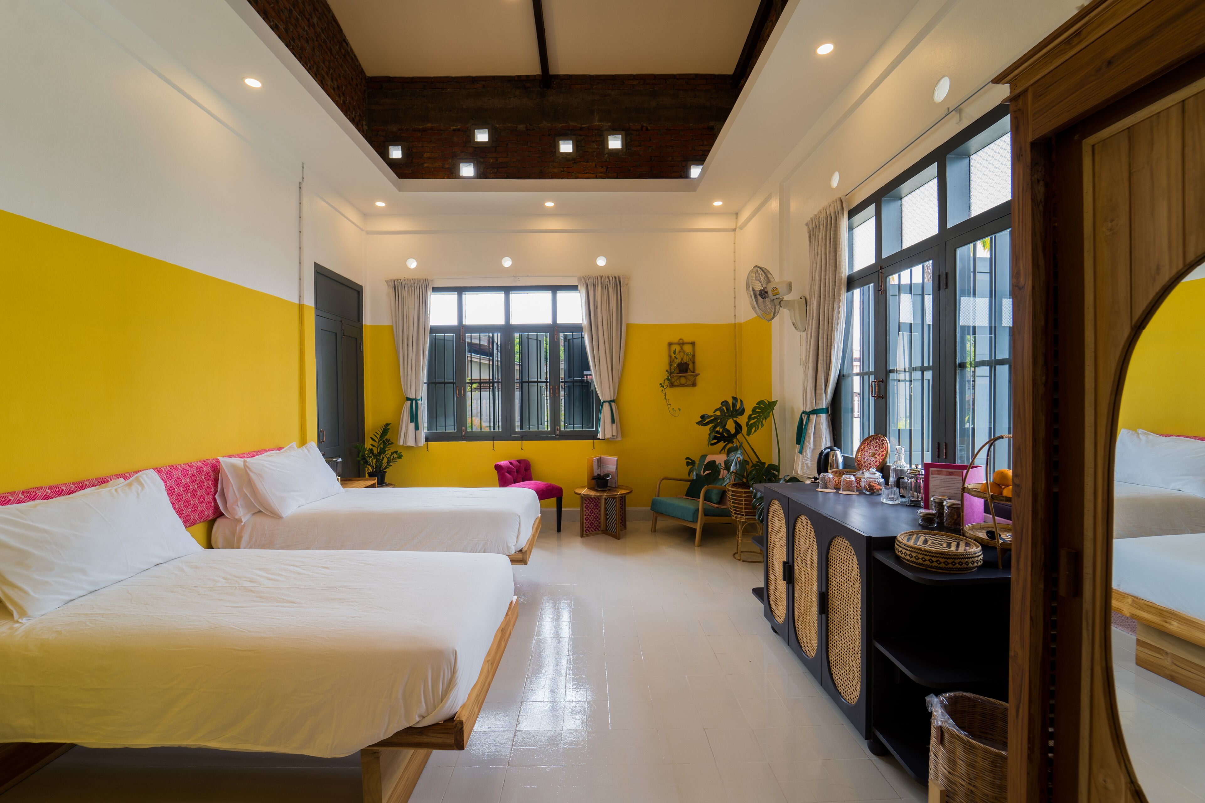 Habitación de hotel con dos camas, una mesita, un ventilador y un ventanal grande.