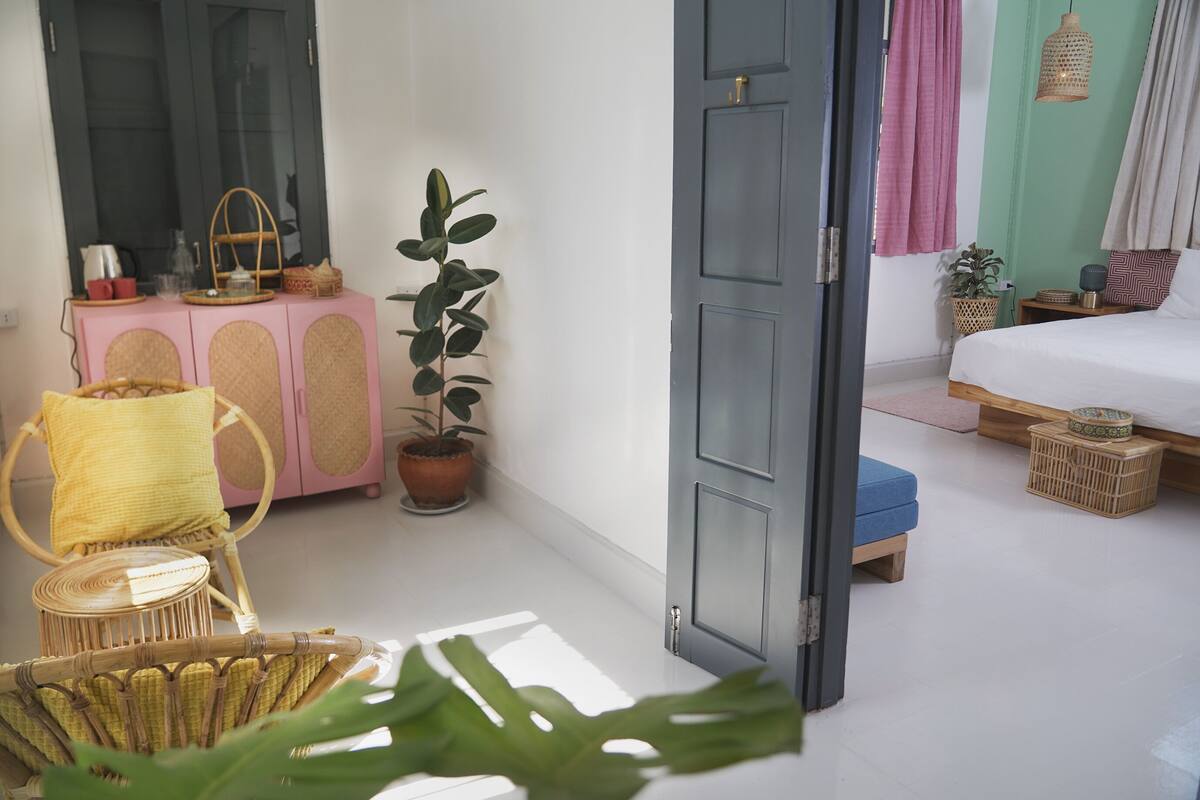 A room with a bed, a small table, a chair, a potted plant, and a cabinet.