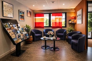 A lobby with a reception desk, seating area, and framed artwork on the walls. - The Originals City Hotel Macon Sud (Chaintre)