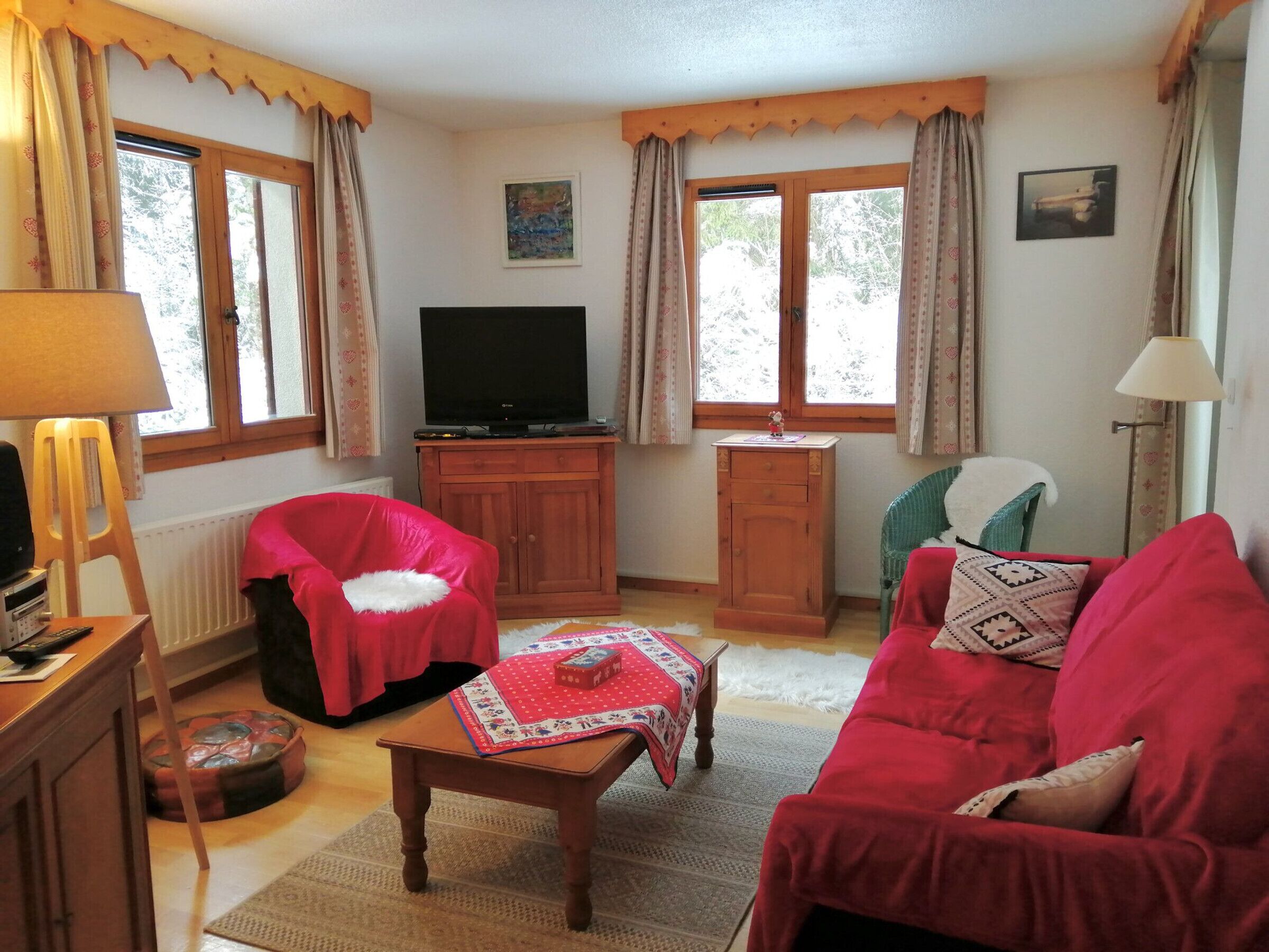 A living room with a red sofa, a wooden cabinet, a television, and a small table with a red tablecloth.