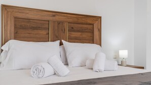 Un lit bien fait, avec du linge de lit blanc et des serviettes pliées, une tête de lit en bois et une table de chevet avec une lampe.