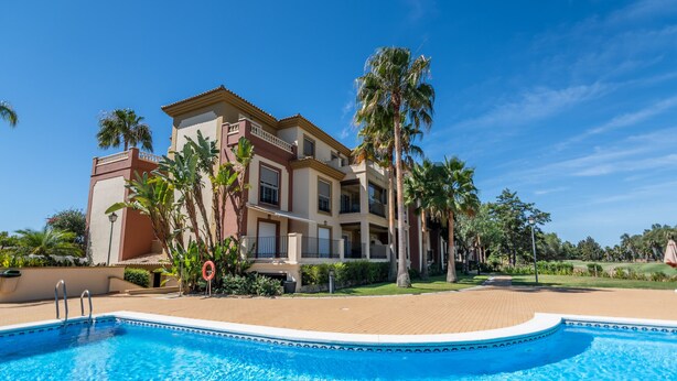 Un hôtel doté d’une piscine, de palmiers et surplombant un ciel bleu azur.