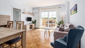 Un salon comprenant un canapé, une table à manger, des chaises, un téléviseur et une porte-fenêtre coulissante donnant sur une terrasse extérieure.