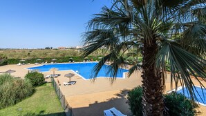 Ein Poolbereich mit Liegestühlen und Sonnenschirmen, umgeben von Palmen und blauem Himmel.