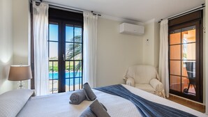 Ein Hotelzimmer mit Bett, Stuhl, Lampe und Blick auf einen Pool.