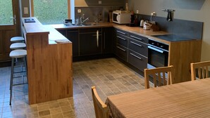 A modern kitchen with a central island, dark cabinetry, a microwave, and a sink. There is a dining area with a table and chairs.