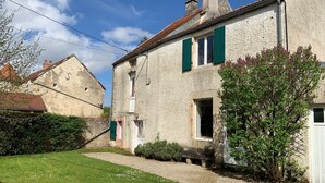 A stone house with green shutters, a gravel path, and a small garden with flowers.