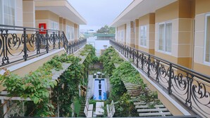 A multi-story building with balconies, a central courtyard with a pool, and a view of the surrounding area. - Hotel Sao Vàng (B'Lao)