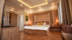 A modern hotel room with a large bed, wooden flooring, a desk, and a nightstand with lamps. - Hotel Sao Vàng (B'Lao)
