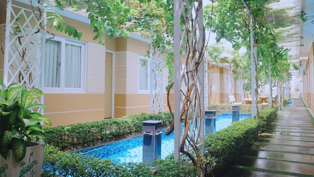 A corridor with a pool, potted plants, and a white lattice structure. - Hotel Sao Vàng (B'Lao)