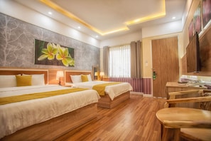A hotel room with two beds, wooden flooring, a large floral painting on the wall, a desk with a chair, and a TV mounted on the wall. - Hotel Sao Vàng (B'Lao)